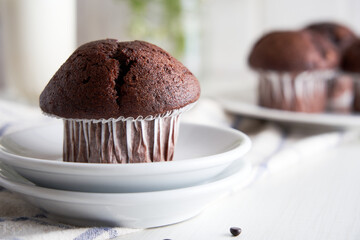 Delicious chocolate muffins in paper cups on a plate on white background.