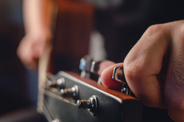 side view man tuning acoustic guitar with hand on headstock in foreground