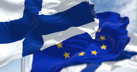 Detail of the national flag of Finland waving in the wind with blurred european union flag in the background on a clear day