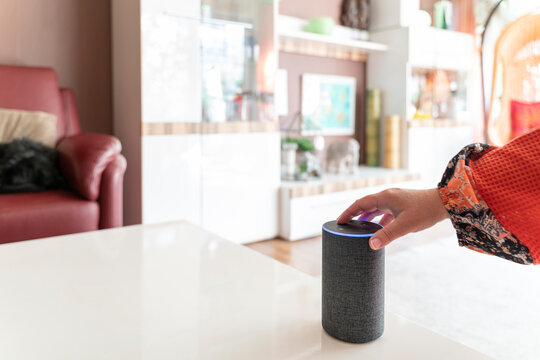 Ein smarter Lautsprecher Assistent steht in einem hellen Wohnzimmer. Eine weibliche Hand bet&auml;tigt eine Taste. Viel Copy Space.