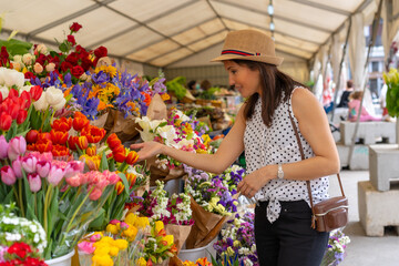 A pretty tourist with a photo camera visiting a flower market, enjoying spring or summer vacation