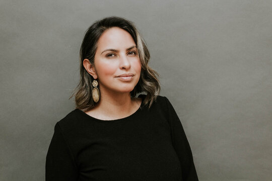 Middle Aged Hispanic Woman Standing In Front Of Gray Background With Inspiring Look