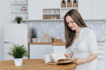 woman reading a book sitting at a table in a cozy kitchen .