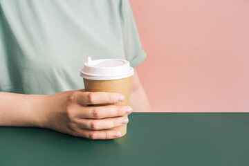 Girl with glass of coffee in her hands sits at green table.