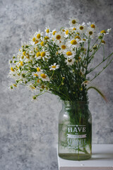 A bouquet of wild daisies in a glass jar on the edge of the table