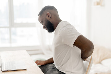 African american guy with back pain massaging lower back pain, suffering from pain while sitting at...