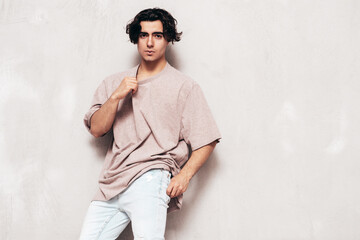 Obraz premium Portrait of handsome confident stylish hipster lambersexual model.Man dressed in over size T-shirt and jeans. Fashion male isolated in studio. Posing near grey wall