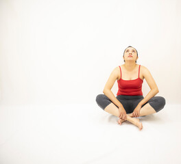 beautiful asian woman in gray sportswear, red blouse, sitting concentrated, head and look up, holding one leg, over white background