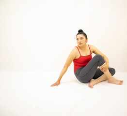 Fototapeta na wymiar athletic woman in gray sportswear, red blouse, sitting contemplating, with open eyes and holding one leg, on white background