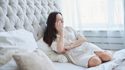 smiling woman talking on her smartphone in her bedroom.