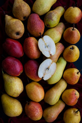 Yellow and red juicy fragrant pears lie on a cherry tablecloth on a black wooden background. One fruit is cut.