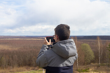 A teenage boy takes pictures on a smartphone of the landscape of a swamp in spring or autumn