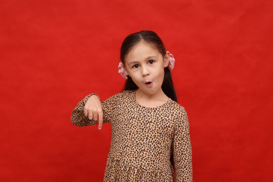Smiling little girl pointing her finger down on a red background