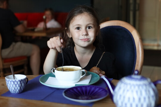 A little girl in a black dress eats soup in a cafe
