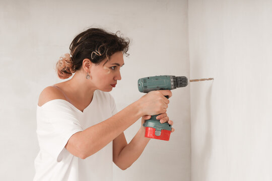 A young woman drills a wall with an electric drill.