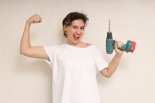 Laughing young woman hold electric drill. Showing biceps, muscles