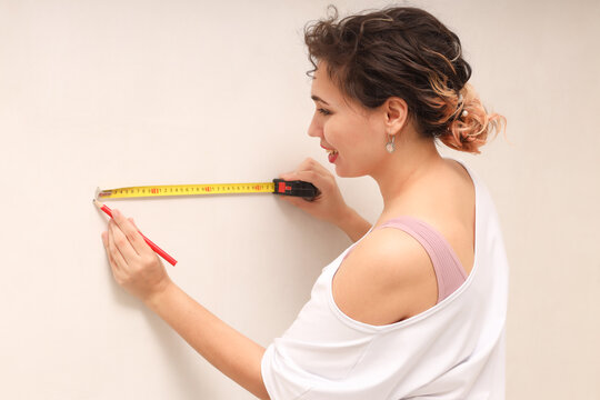 A woman with a meter in her hands, measuring the dimensions of the wall - the concept of home improvement with her own hands