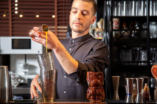 Professional barman pouring alcohol drink into jigger during cocktail preparation