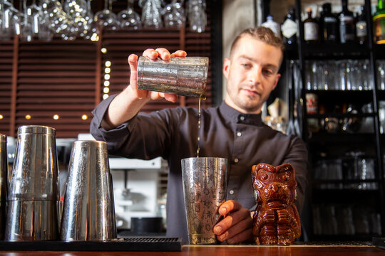 Serious young barman preparing cocktail in shaker in bar