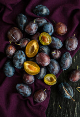 Dark ripe juicy plums lie on a purple tablecloth, which lie on a black wooden background. Several boats are cut.