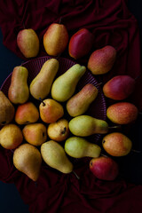 Yellow and red juicy fragrant pears lie on a cherry plate on a dark cherry tablecloth.