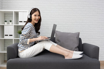 Happy young Asian woman work on laptop computer at home living room, Looking at camera