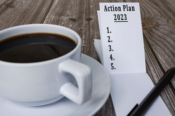 Note book with action plan 2023 text and coffee on wooden desk.
