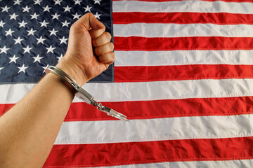 caucasian hand cuffed with silver metal handcuffs over US flag background.
