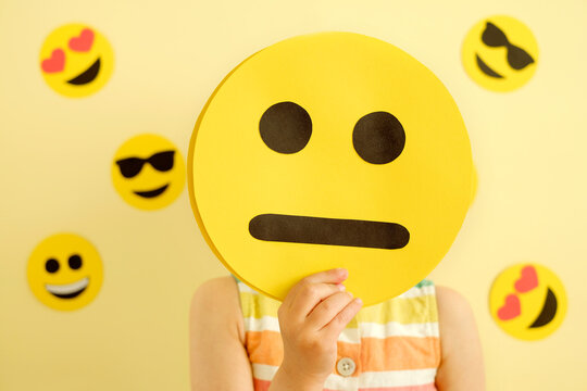 A human holds in his hand a mask with a emoticon with an unhappy embarrassing face.