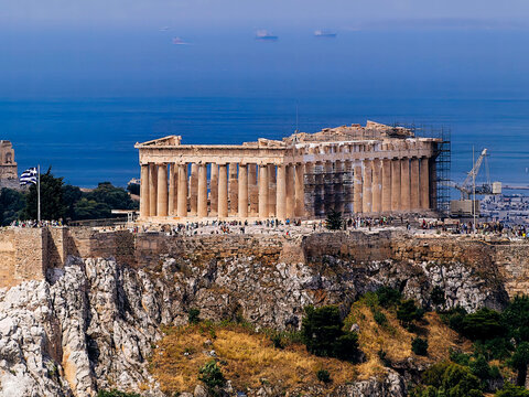 A view of Parthenon ancient Greek temple standing on Acropolis hill, with Plaka on the footsteps, and the blue Saronic sea in the far background.
