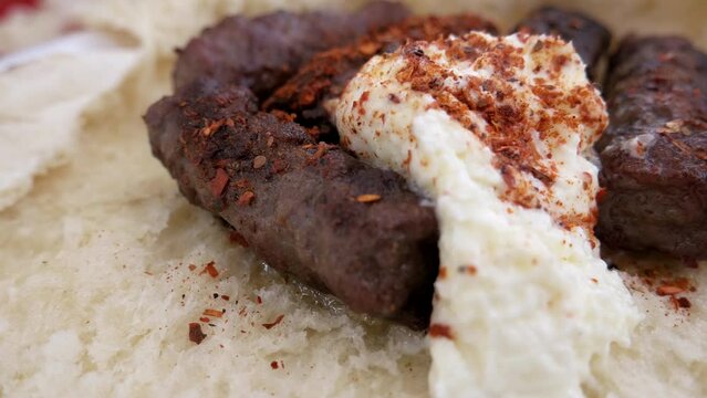 Cevapi - a traditional minced meat dish from the grill, served on a bun with creamy kaymak and paprika powder. Close up, macro, handheld shot 