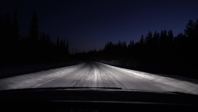 First Person View Driving a Car on a Snowy Road in a Nighttime Forest.