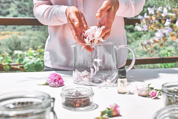 Woman preparing roses water with pink rose petals in glass bowl. Skin care and spa, natural beauty treatment, homemade cosmetics.