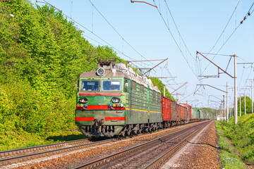 A powerful green electric locomotive pulls a long train of wagons loaded with coal to the railway...