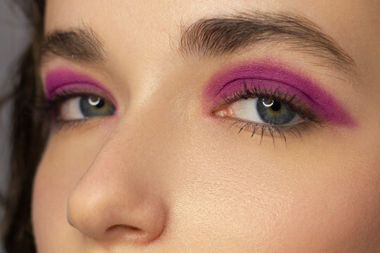 Close eye with colorful eyeshadow. Macro shot of opened human female eye. Woman with evening beauty makeup. Girl with perfect skin and eyebrow. Women cosmetics, extremely long eyelash and pink glitter