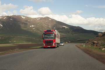 A big truck with a red trailer with space for text on a countryside road in motion against a blue sky with clouds