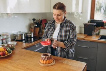 Happy Woman making homemade cake with easy recipe, sprinkling powdered sugar on top. Young redhead girl pastry chef making chocolate cake in the kitchen. Baking Concept
