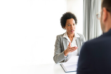 Businesswomen talking to client in her office. African American HR manager sitting at desk in office talking with a potential new employee during job interview. Copy space