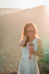 Fototapeta na wymiar Stylish bride standing back with wedding bouquet on beautiful landscape of sea and mountains on sunset