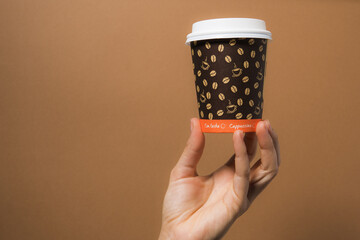 Mano sosteniendo vaso de café sobre fondo marron