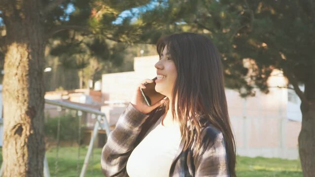 Mujer joven camina y habla por tel&eacute;fono en una ciudad de Latinoam&eacute;rica al atardecer. Concepto de personas y estilo de vida.