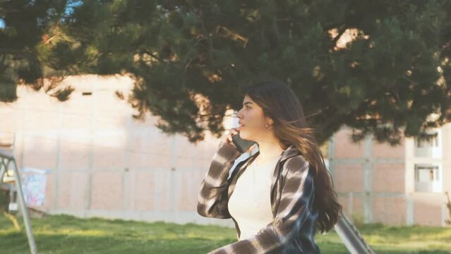 Mujer joven camina y habla por tel&eacute;fono en una ciudad de Latinoam&eacute;rica al atardecer. Concepto de personas y estilo de vida.
