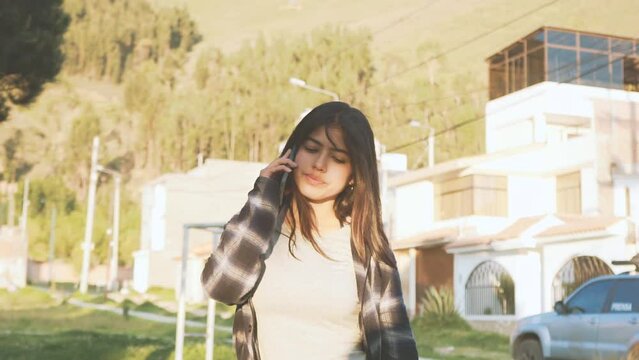 Mujer joven camina y habla por tel&eacute;fono en una ciudad de Latinoam&eacute;rica al atardecer. Concepto de personas y estilo de vida.