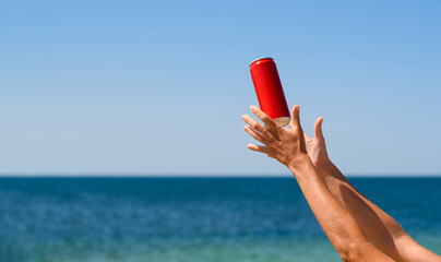 Red jar with a cold drink and female hands on the background of the sea.