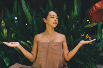 Attractive Asian woman in towel raising hands meditate while waiting for spa procedure at nature, charming Korean female with closed eyes relaxing and resting during weekend leisure for herself