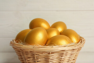 Shiny golden eggs in wicker basket on light background, closeup