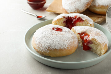Delicious donuts with jelly and powdered sugar on light grey table, closeup