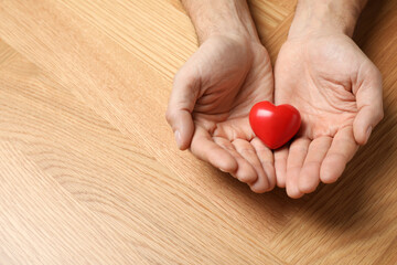 Man holding red heart in hands at wooden table, closeup. Space for text