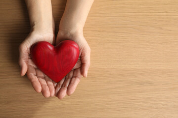 Elderly woman holding red heart in hands at wooden table, top view. Space for text