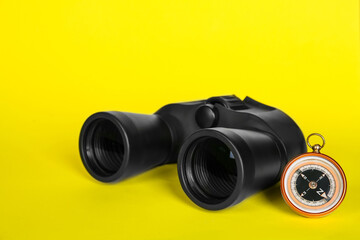 Modern binoculars and compass on yellow background